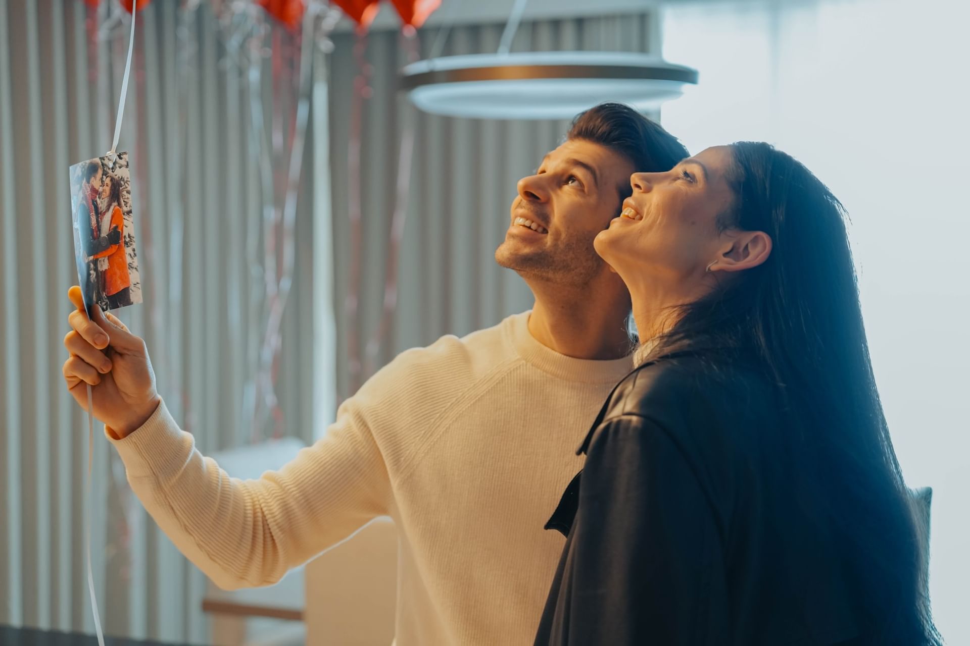 Couple smiling up at a photo hanging from a balloon ribbon, under a round ceiling light at Hotel X Toronto