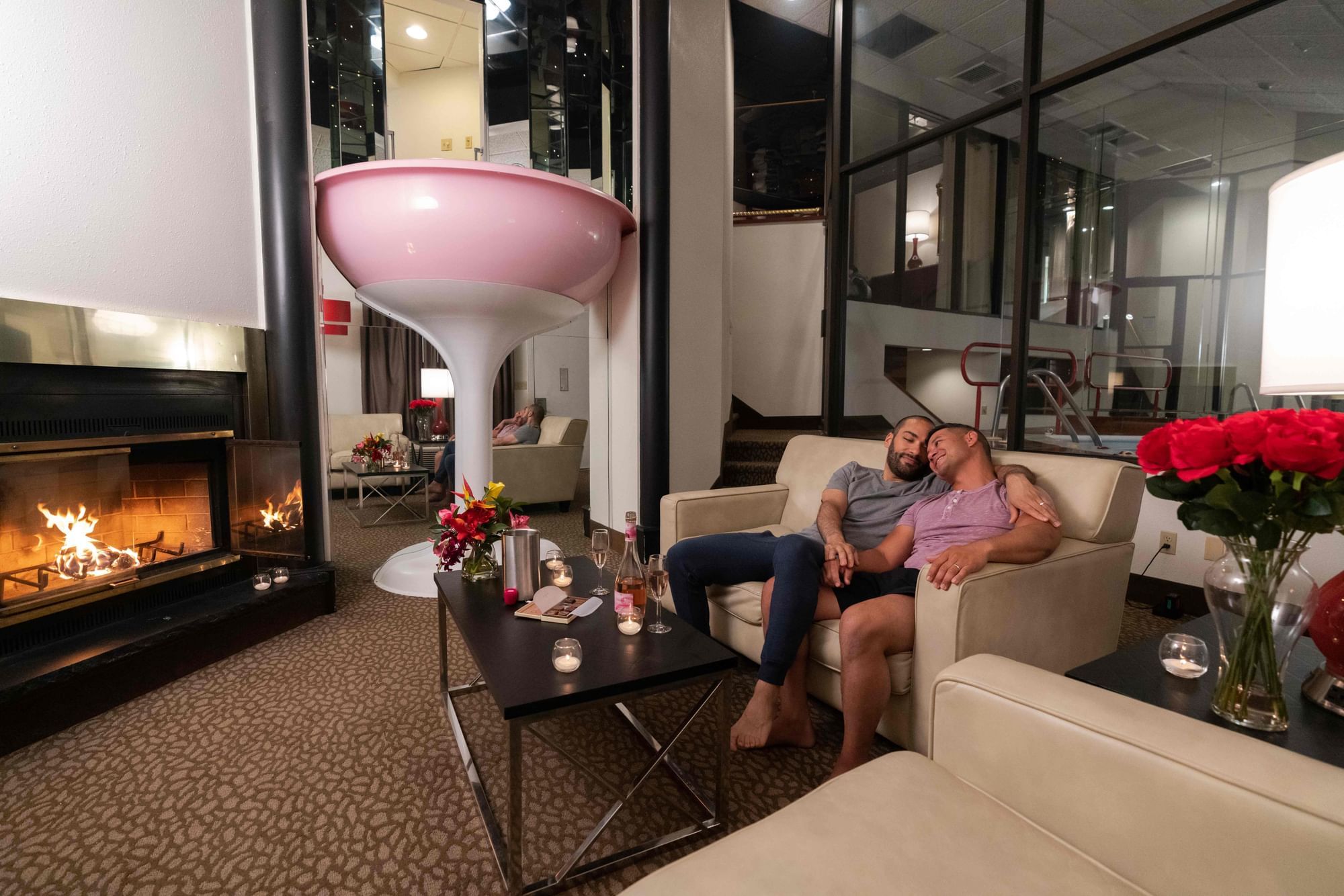 Two men sit together on couches in a cozy living room by a Champagne Tower and decorative elements at Cove Pocono Resorts