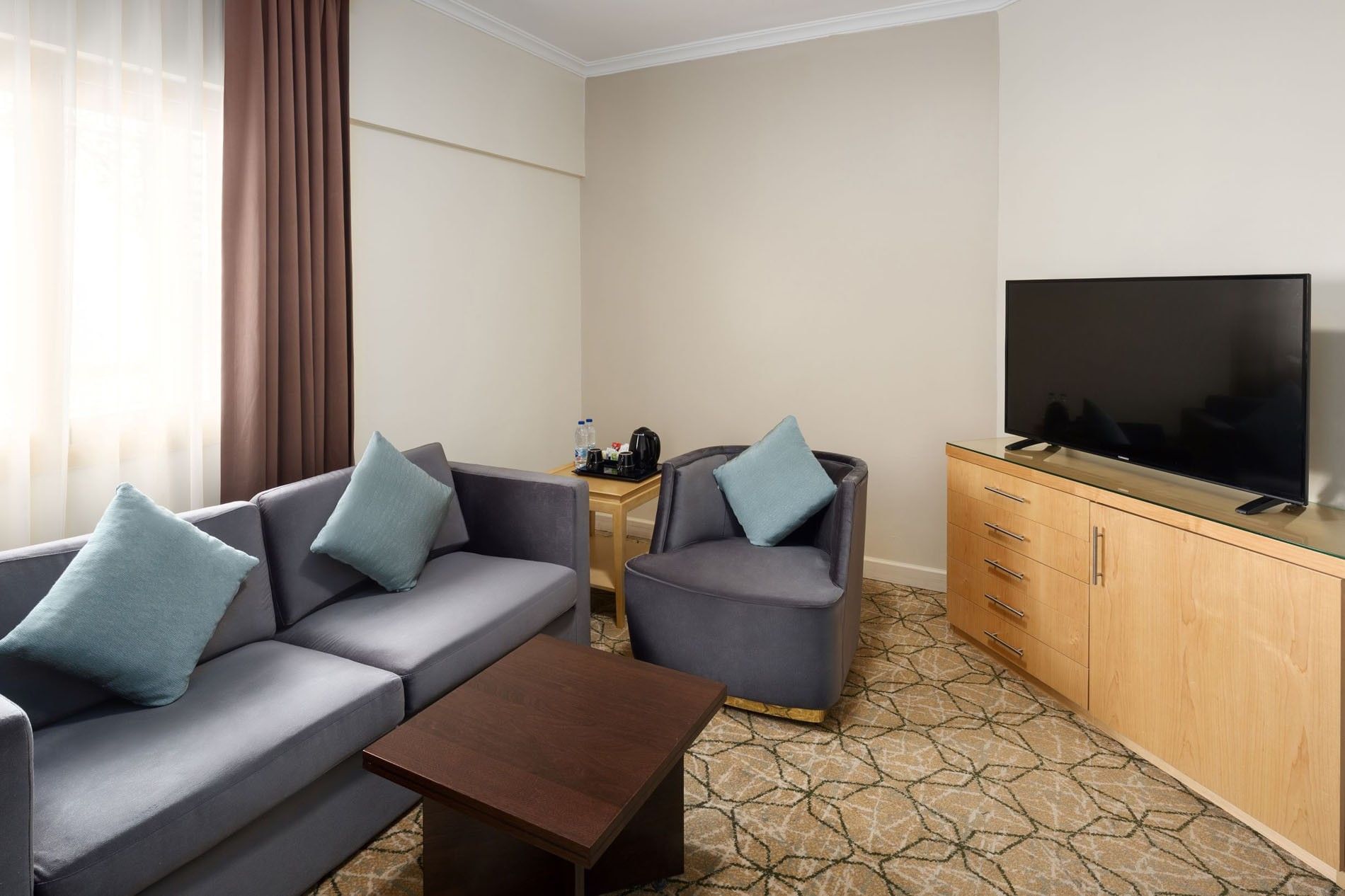 Seating area with grey sofa & blue cushions, and a flat screen TV on a dresser at Saja Warwick Madinah