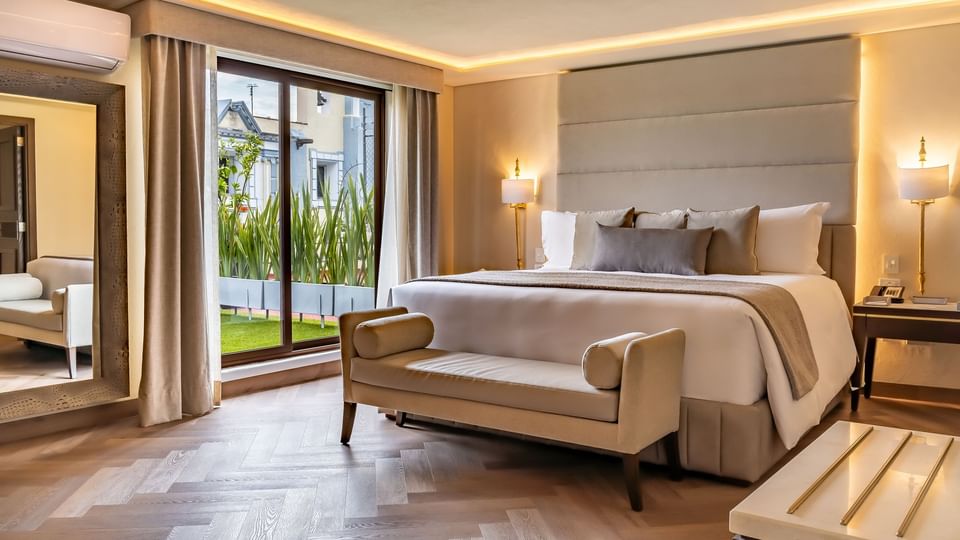 Habitación de hotel de lujo con cabecera grande beige y ventana con vista a jardín en Quinta Real Puebla