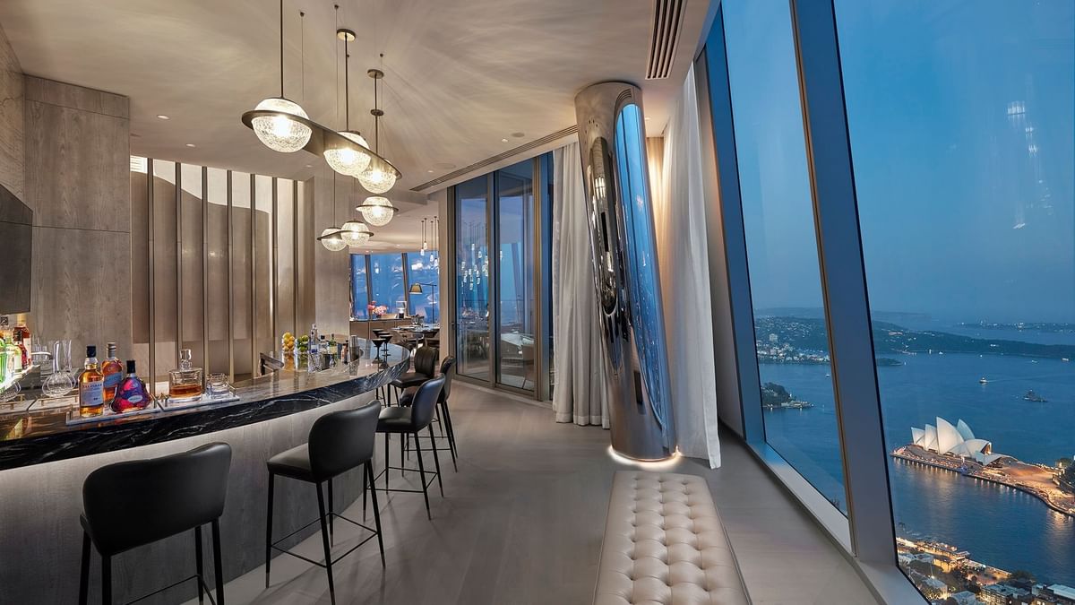 Bar area with stools, pendant lights, and large windows overlooking a cityscape in Crown Presidential Villa at Crown Hotels