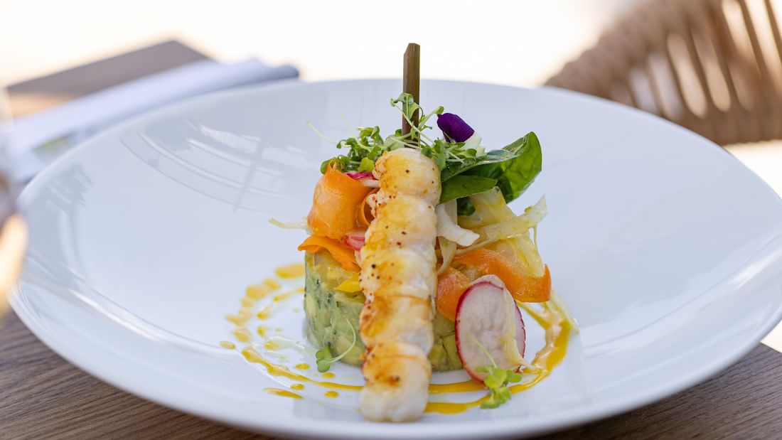 Plat de fruits de mer et légumes sur une assiette blanche avec une sauce jaune.