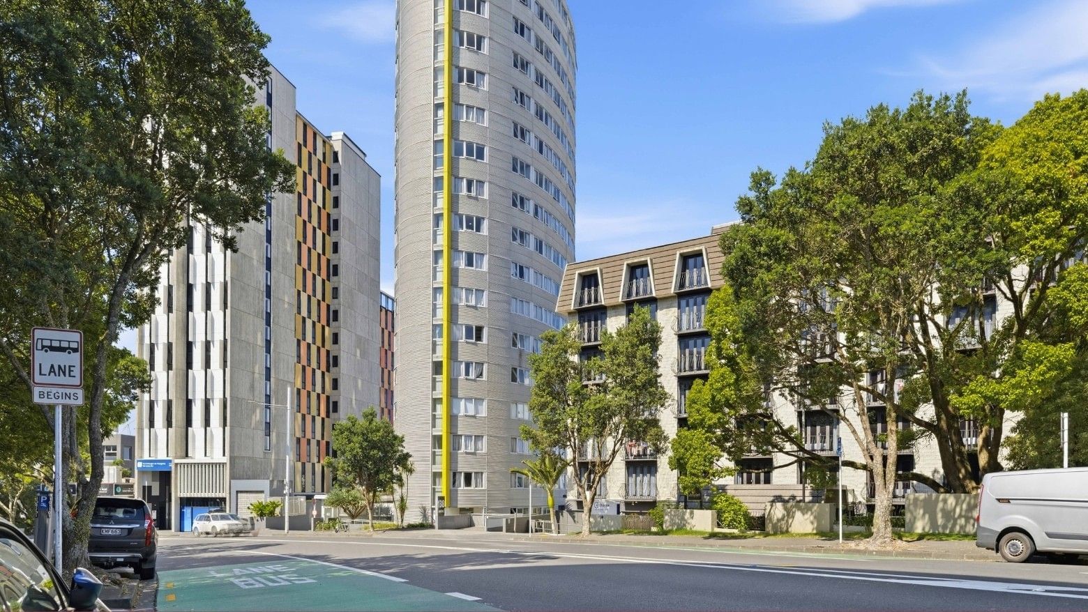 Street view of the Student Living Auckland - Beach apartment building with trees and cars.