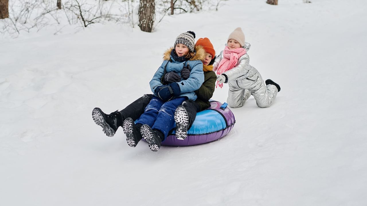 Three children riding an inflatable sled on snowy ground at Eastlink Park.