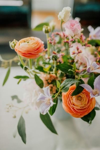 A bouquet of orange and pink flowers with greenery set on a white surface. Buy yourself flowers to celebrate Singles Awareness Day.