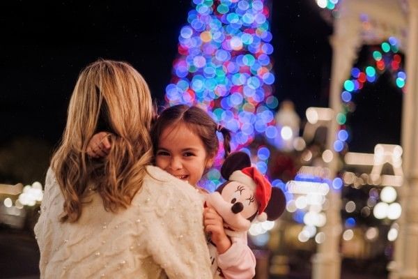 A girl holding a Minnie Mouse toy smiles over her mother's shoulder at Mickey's Very Merry Christmas Party. 