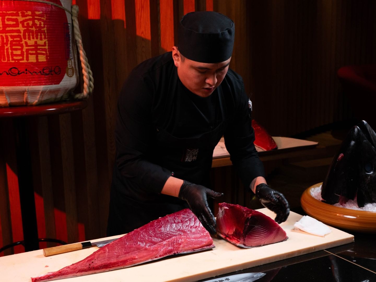 Chef wearing black attire and gloves skillfully slices a large piece of tuna on a wooden board at Camino Real