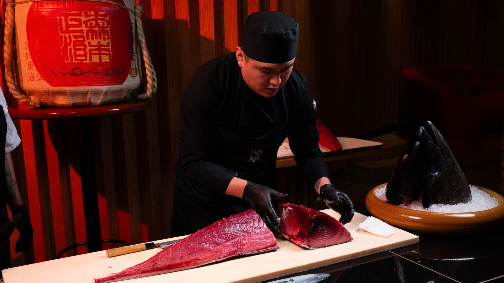 Chef wearing black attire and gloves skillfully slices a large piece of tuna on a wooden board at Camino Real