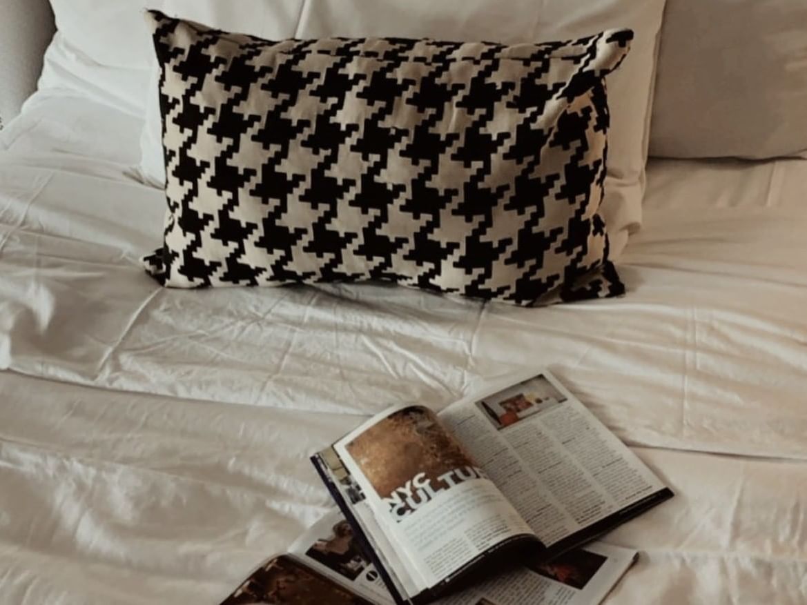 Houndstooth print throw pillow on a large bed with magazines in a New York City hotel room