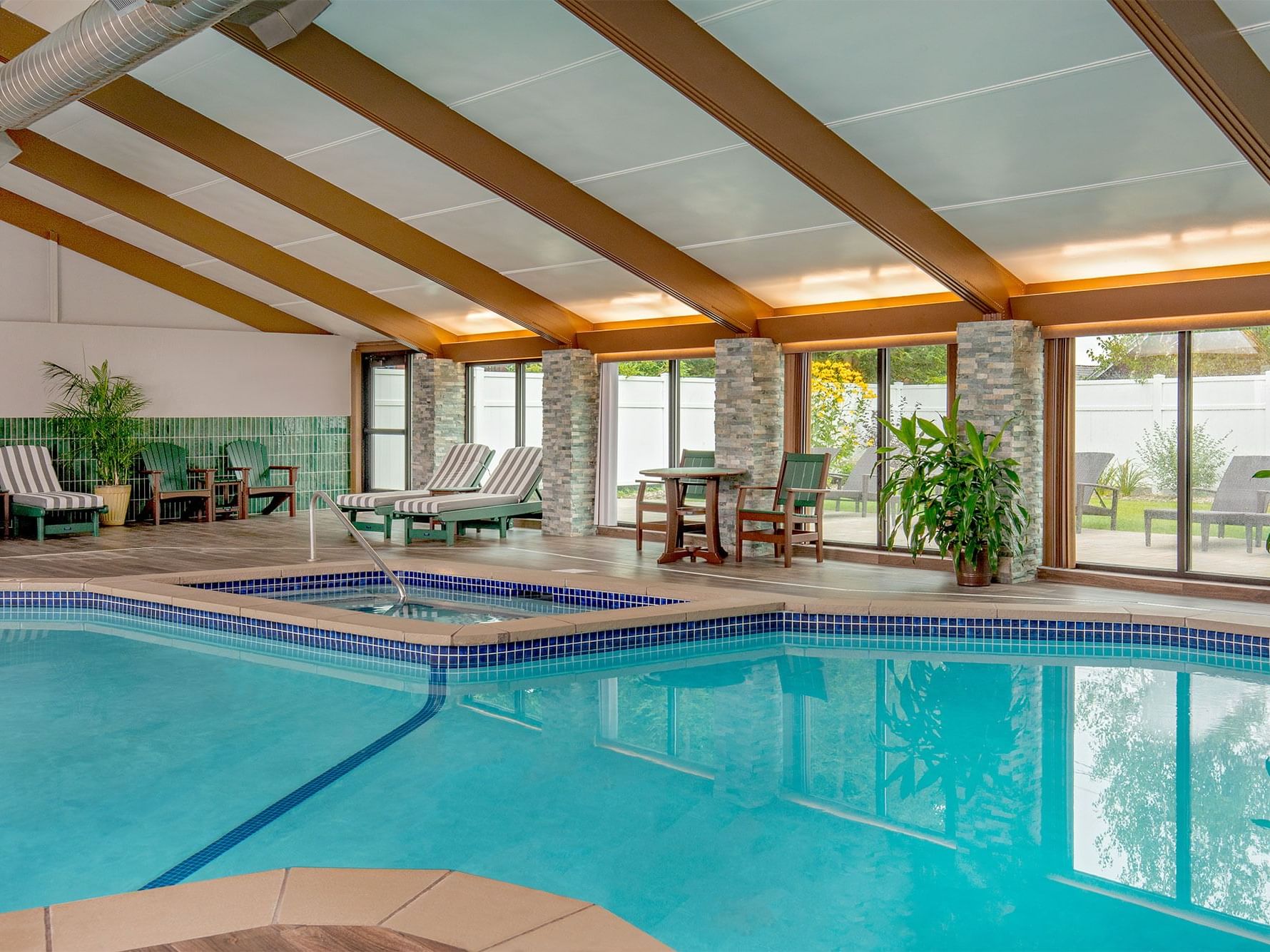 Indoor pool withy hot tub, seating, and indoor plants.