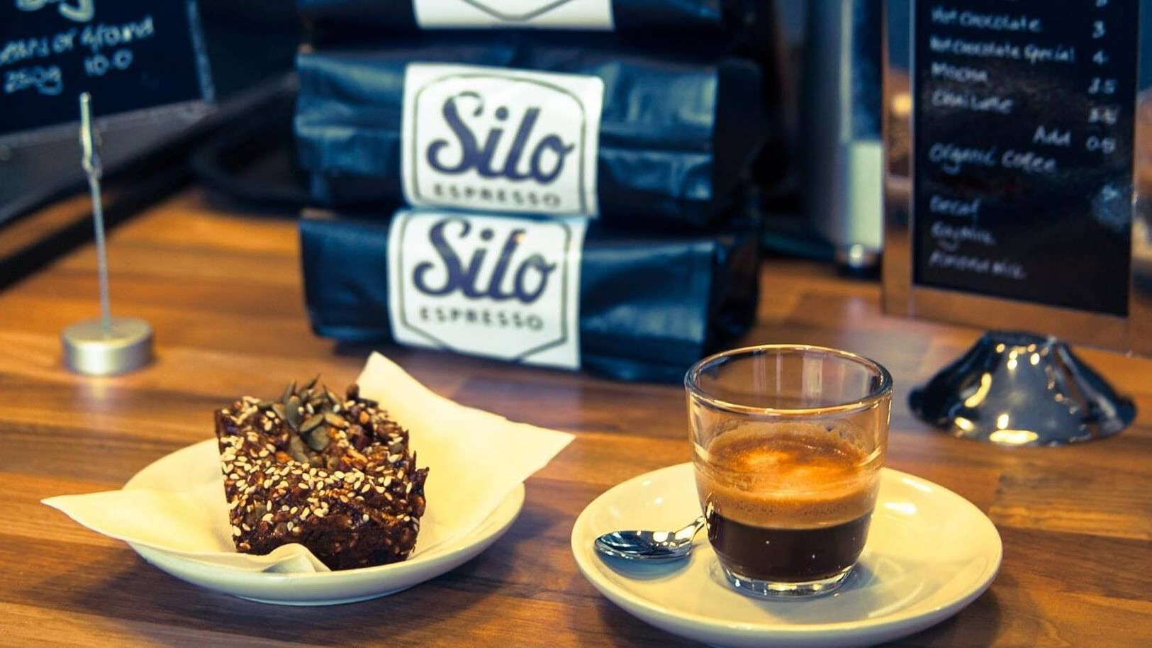 Espresso glass on a saucer by a seed brownie under coffee bags at Elysium Manly, an apartment hotel in Manly