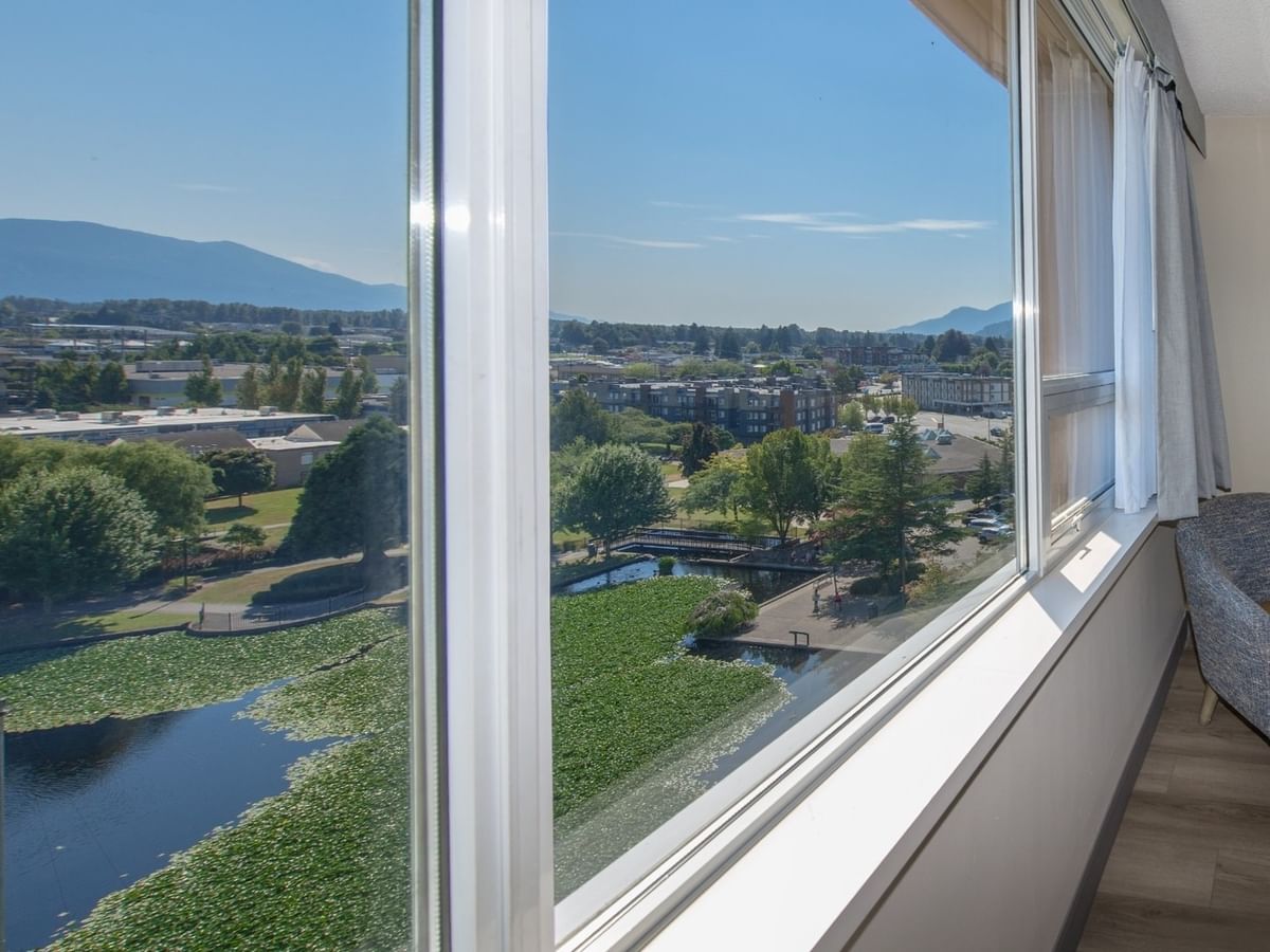 Panoramic view from a large window of a pond, surrounded by greenery and mountains.