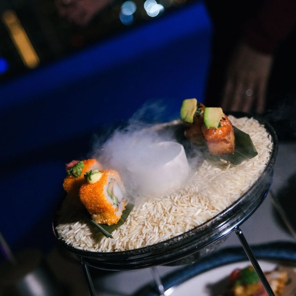 Gourmet sushi topped with avocado served over dry ice and a bed of rice on a glass platter at Malibu Sky Lounge & Bar