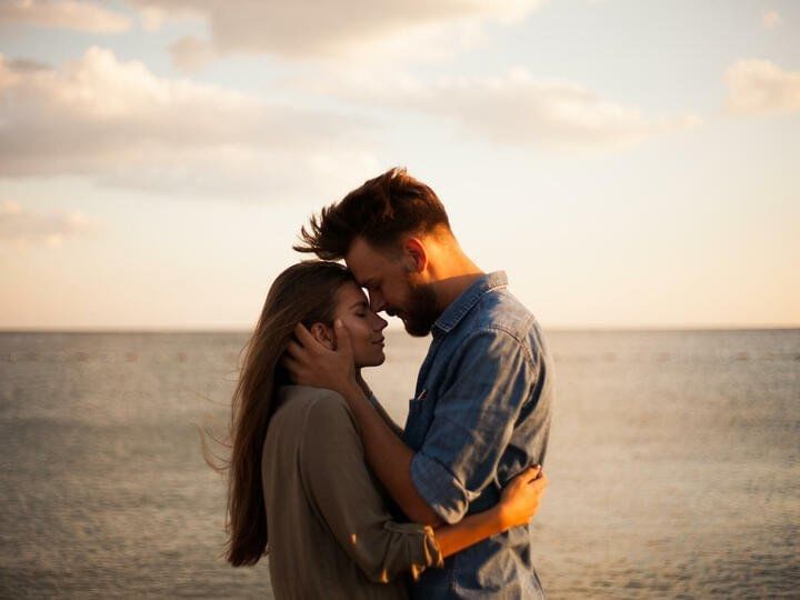 A romantic couple hugging on the beach as the sun sets in the background at Live Aqua Beach Resort