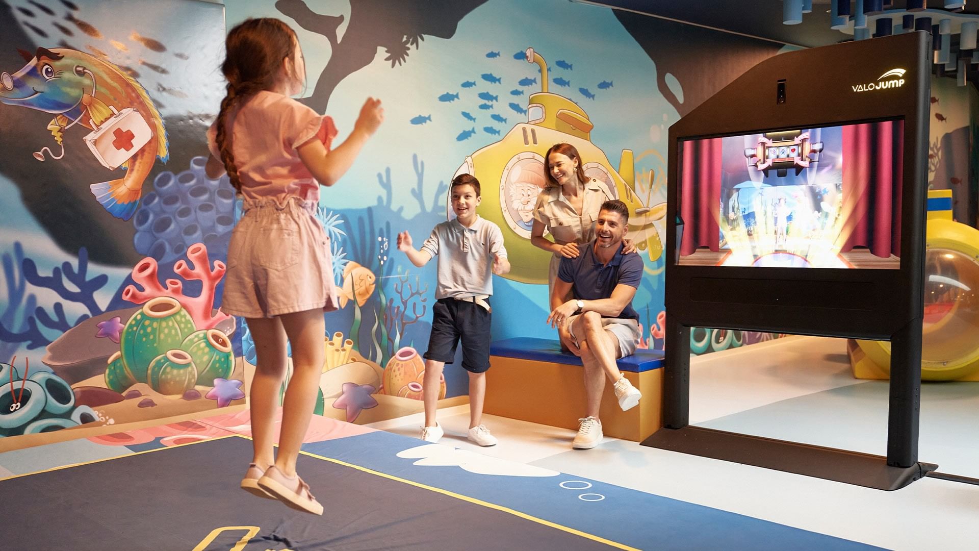 Family of four playing a virtual reality game in an ocean-themed room with a large screen.
