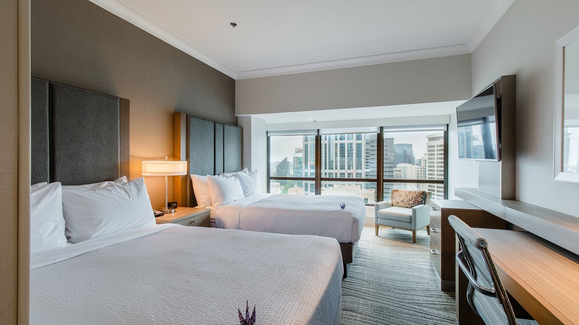 A hotel room with two beds, a desk, a chair, and a TV on the wall.