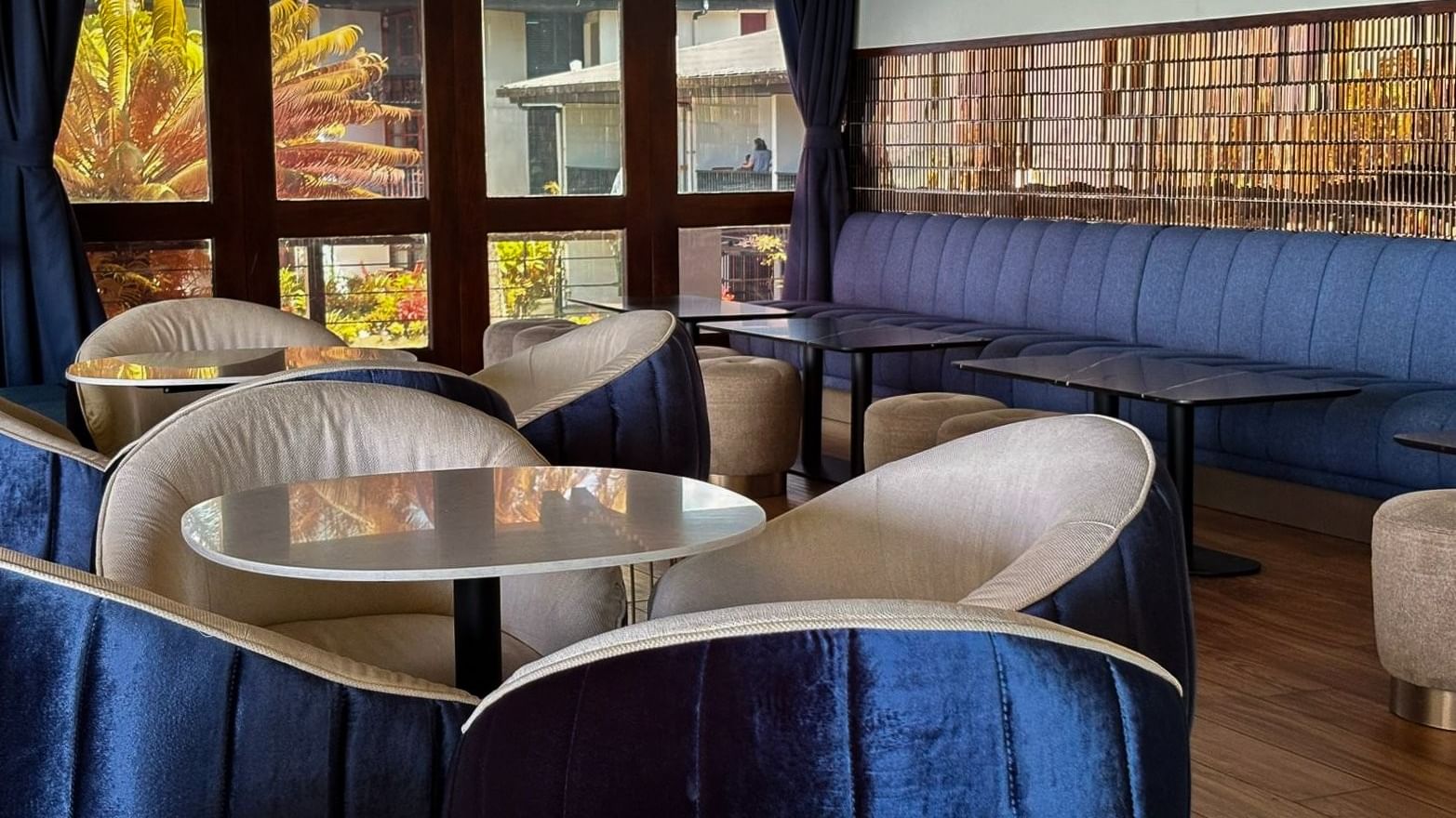 Velvet chairs by round tables under modern wall lights near a blue sofa in Hibiscus Lounge at Warwick Fiji Resort and Spa