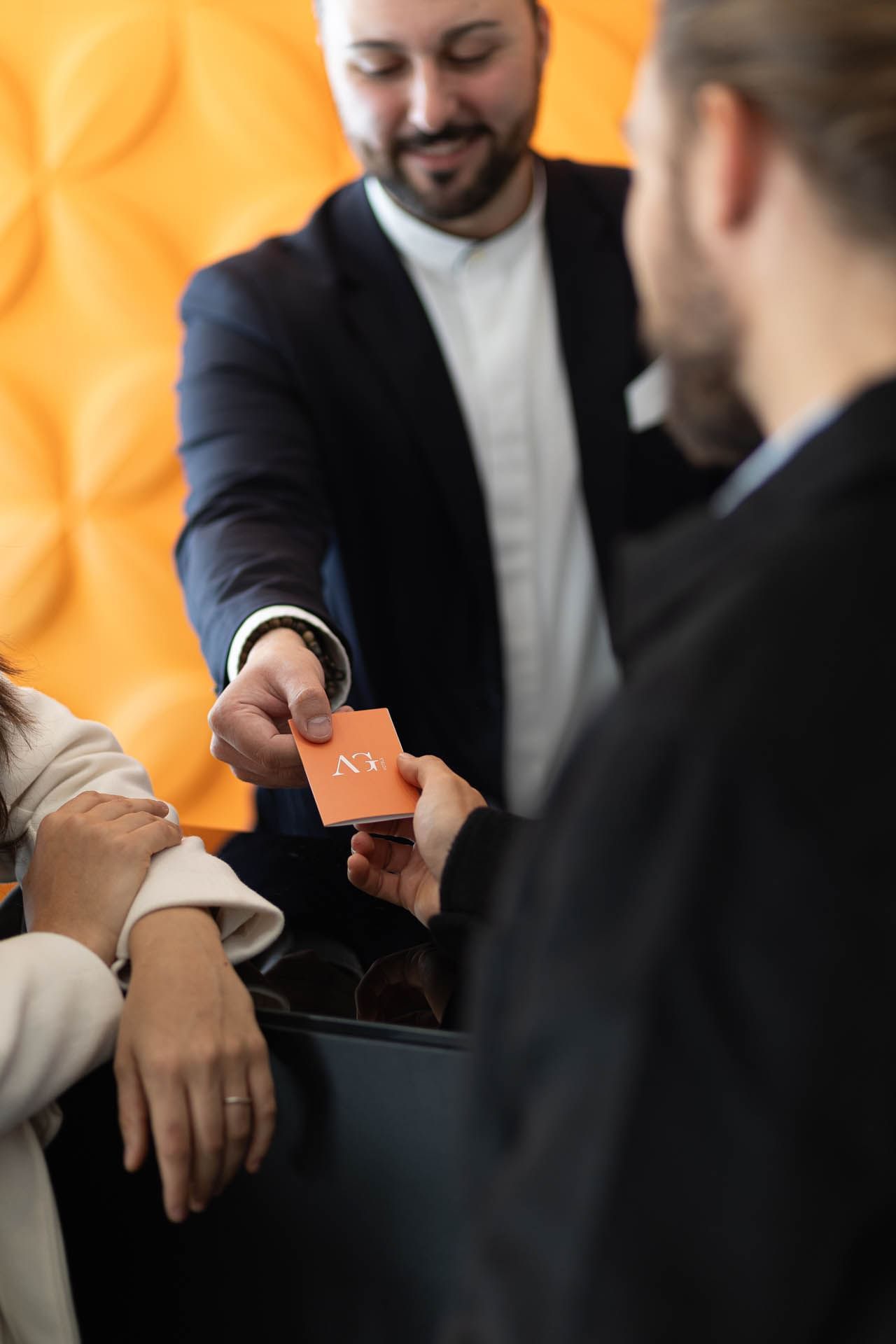 Hand extends an AG business card to another person, with a blurred figure at The Republic Hotel