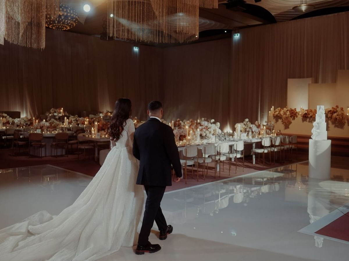 Kayla and JJ entering a wedding hall with decorated tables at Crown Towers Perth