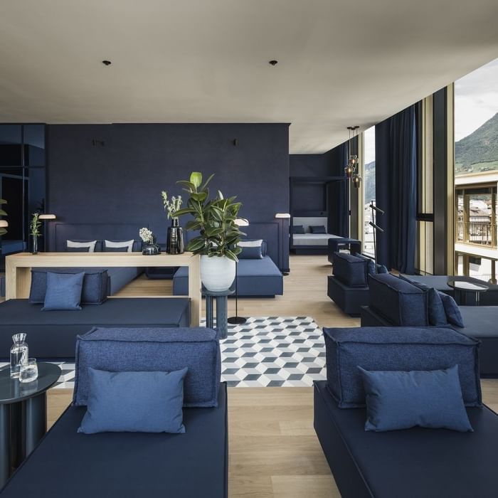 Blaues Wohnzimmer mit großen Fenstern, Loungemöbeln und einer Pflanze in einem weißen Topf.