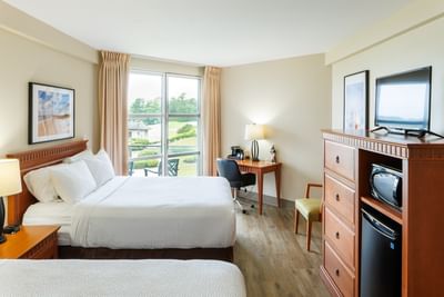 Beds by a wooden dresser surrounding a chair setup at Rodd Brudenell River Resort, one of the premier places to stay in PEI