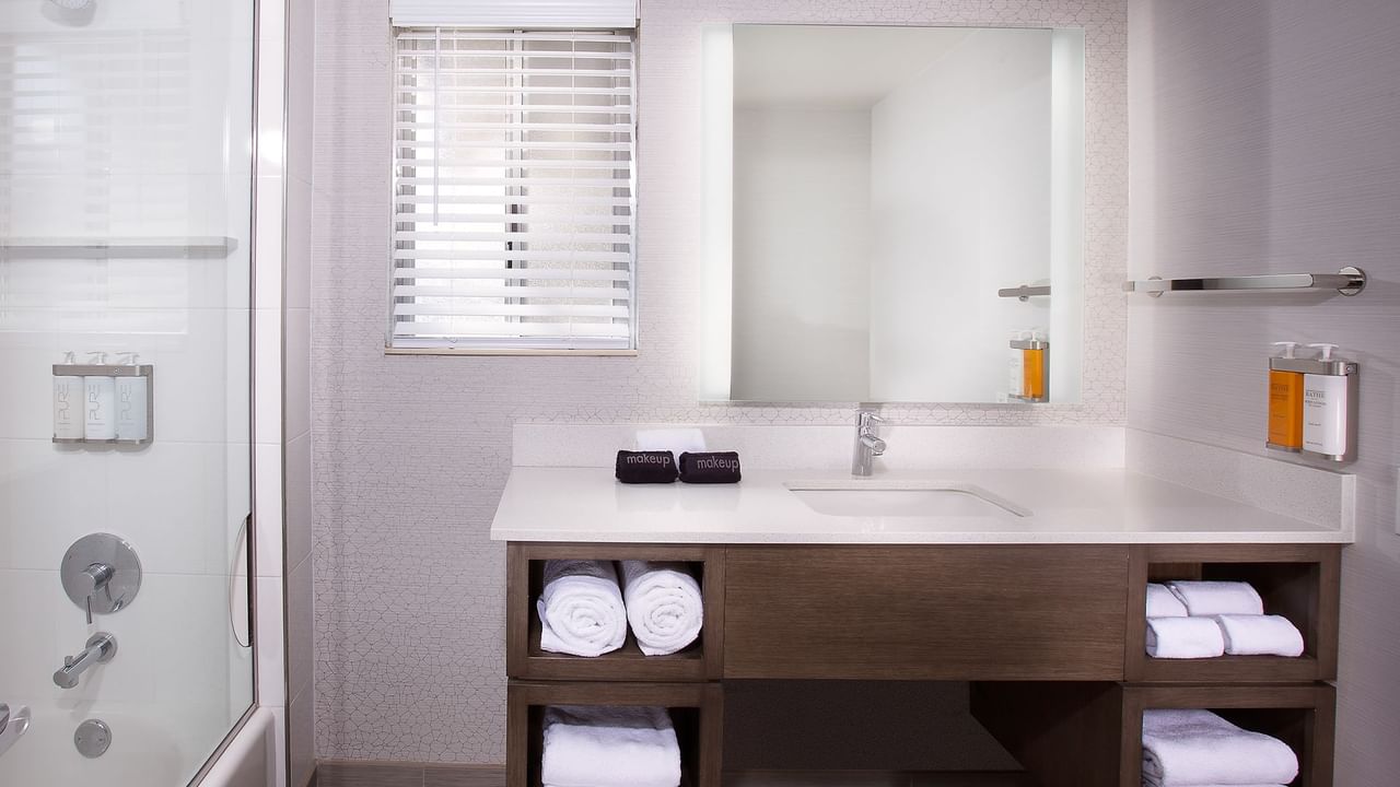 A bathroom featuring a sink, a large mirror, shower, towels and soap