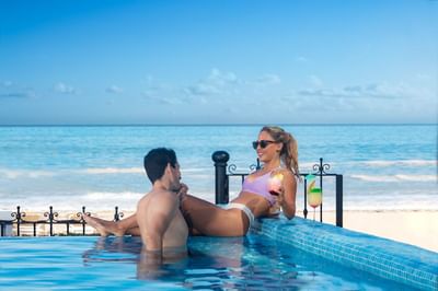 Couple relaxing in infinity pool with tropical cocktails overlooking the ocean at Playa Los Arcos Puerto Vallarta 2023