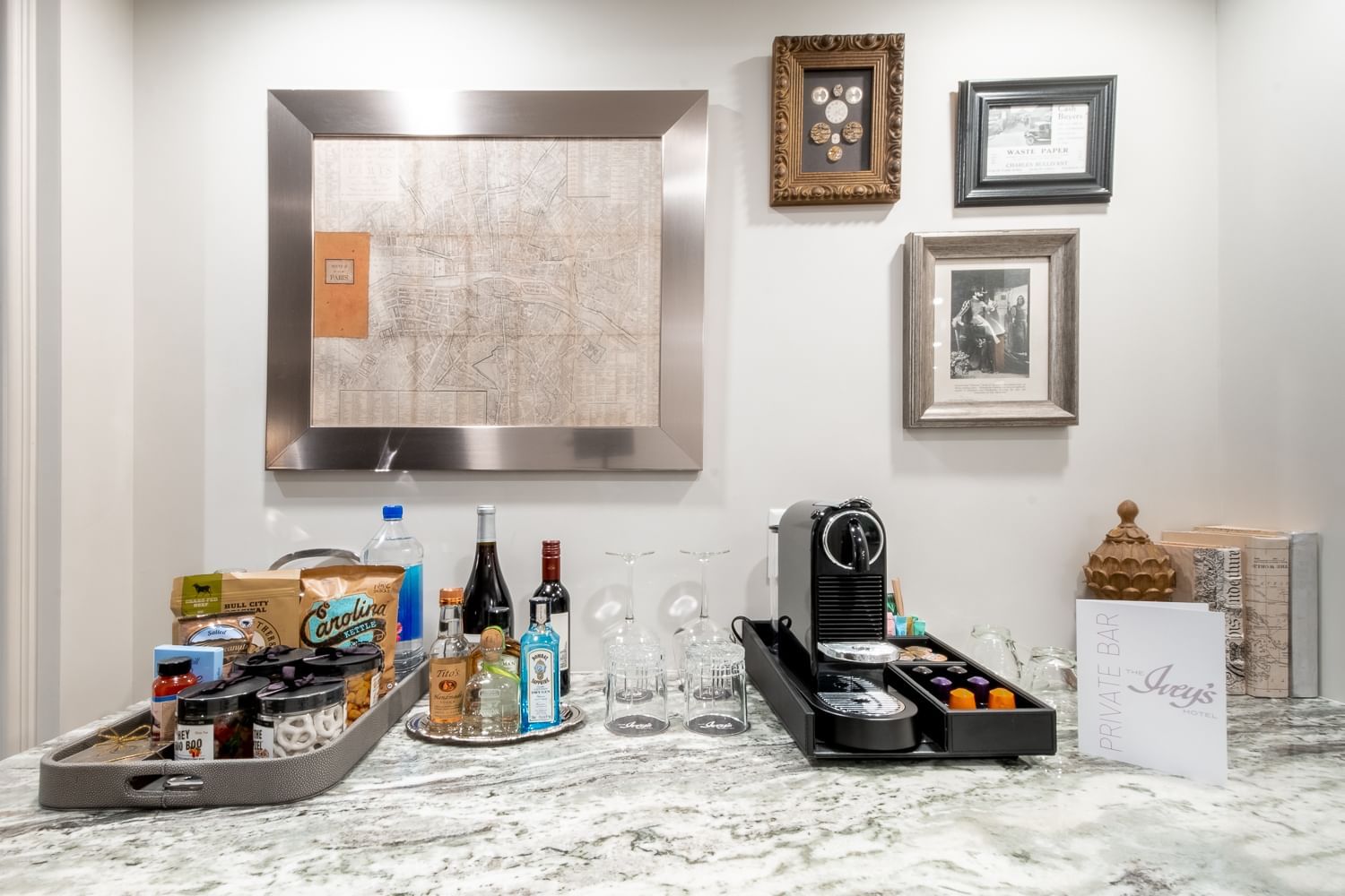 A hotel room countertop with a mini bar, coffee machine, and framed pictures on the wall.