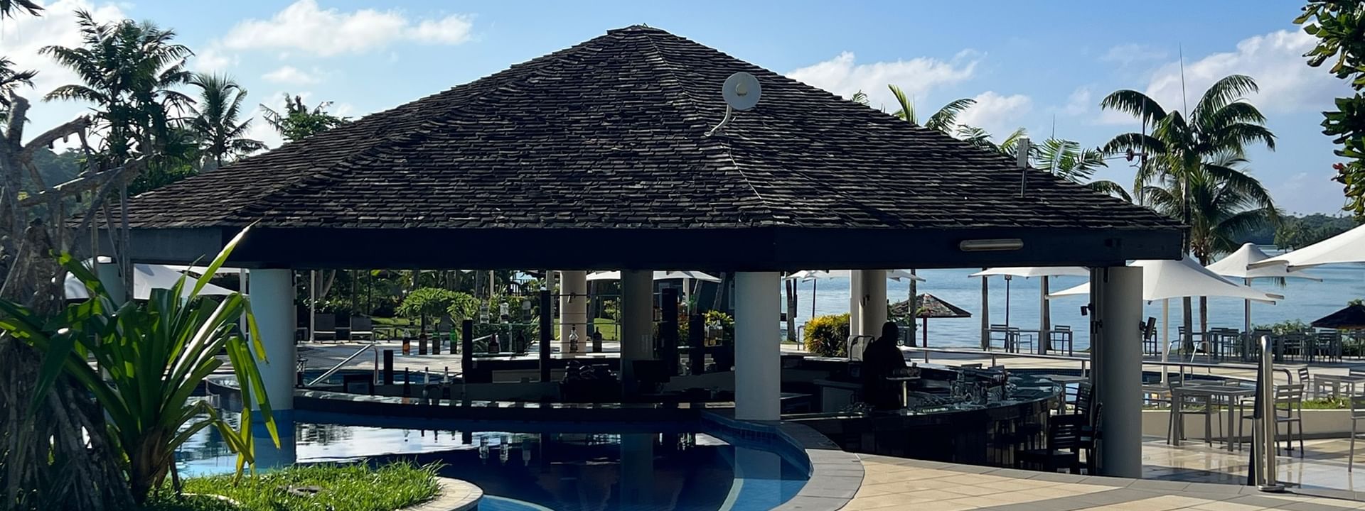 Outdoor Pool Grill & Bar with a thatched roof by a sun-drenched patio and palm trees at Warwick Le Lagon - Vanuatu in Efate