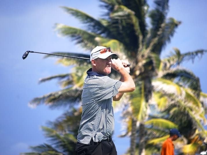 Golfer in a striped polo shirt swinging his golf club under tropical palm trees near the Jamaica Pegasus Hotel