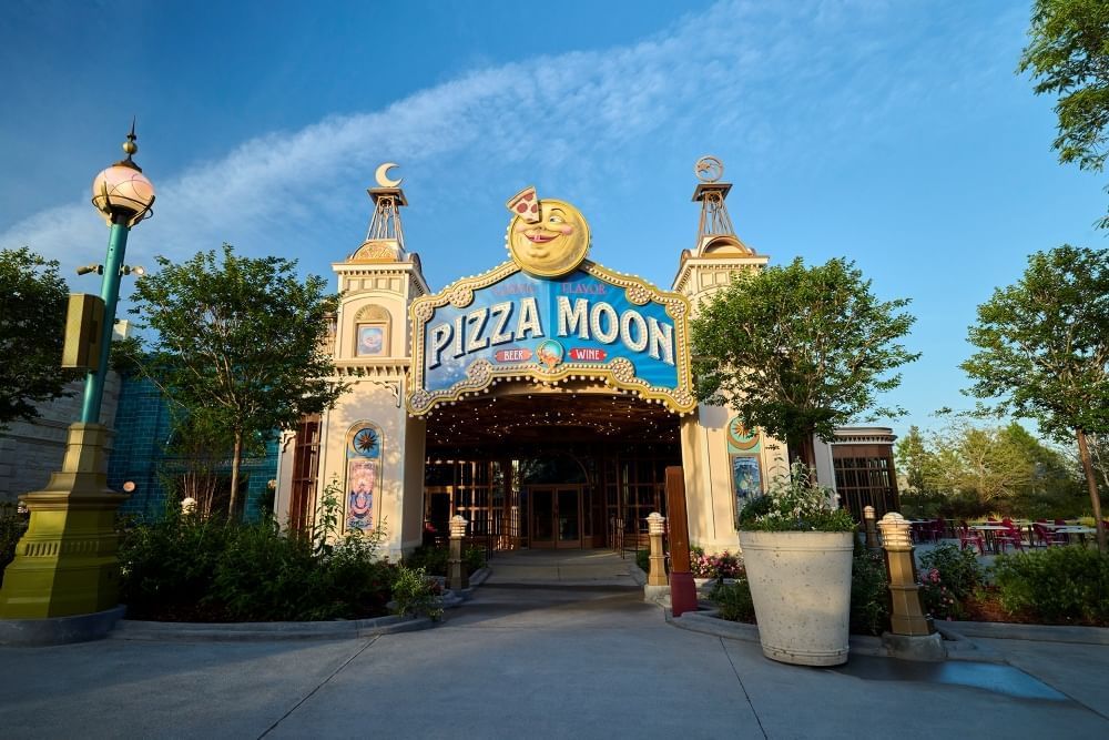 The exterior of a restaurant with a large blue sign that reads Pizza Moon, with a smiling moon image and a slice of pizza in its eye.