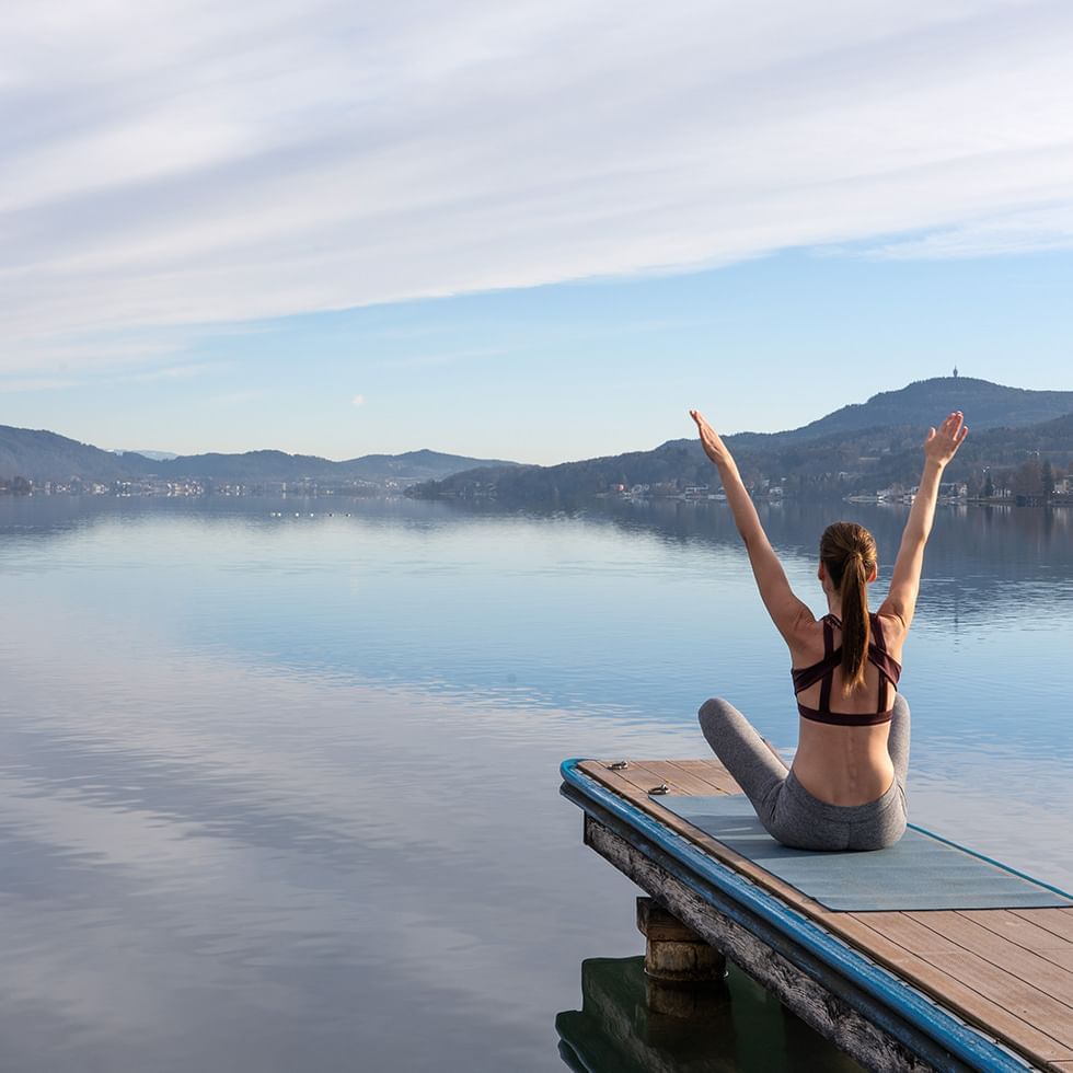 Woman doing yoga on a deck by the lake at Falkensteiner Hotels