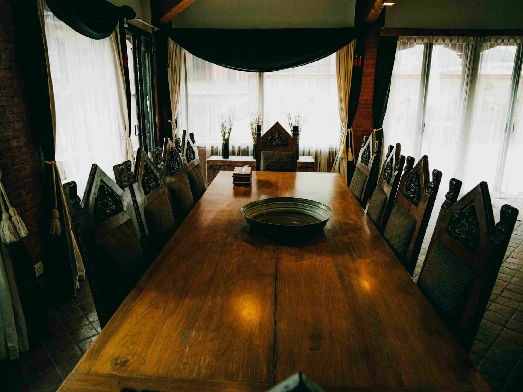 Wooden table surrounded by ornate chairs, with natural light streaming through sheer curtains at Dwarika's Hotel Kathmandu