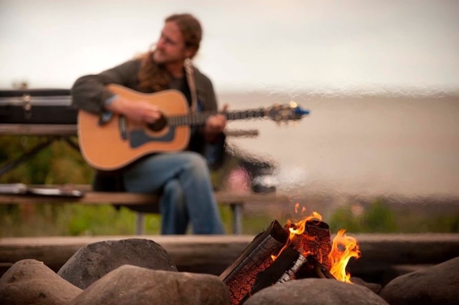 man playing guitar by bonfire