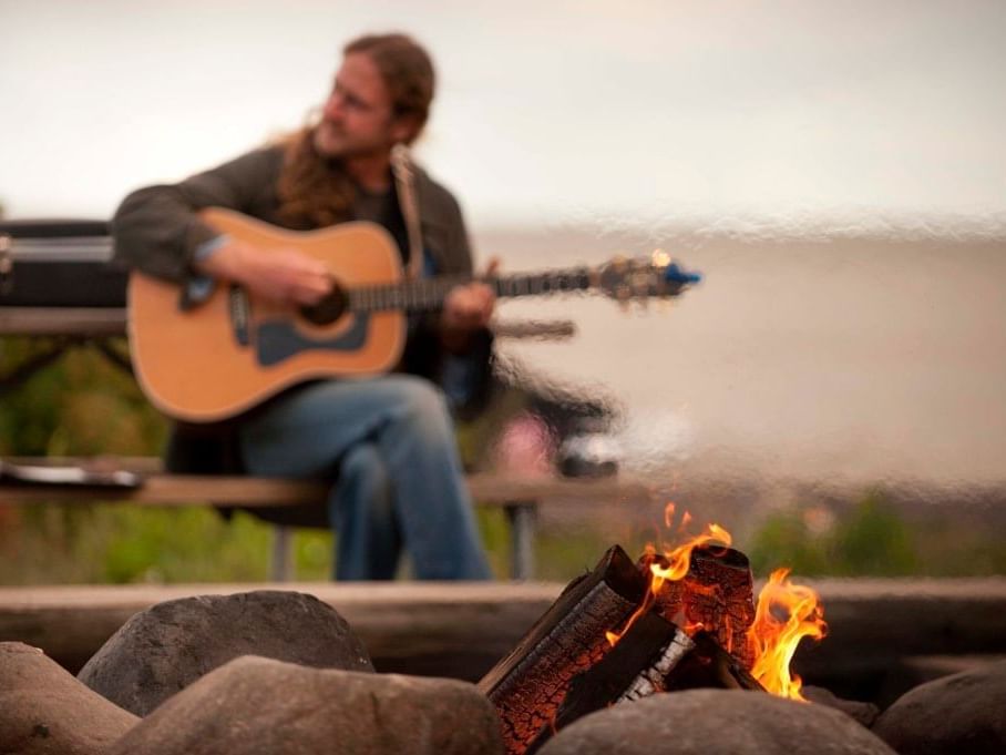 A man playing guitar by a bonfire at Lutsen Resort