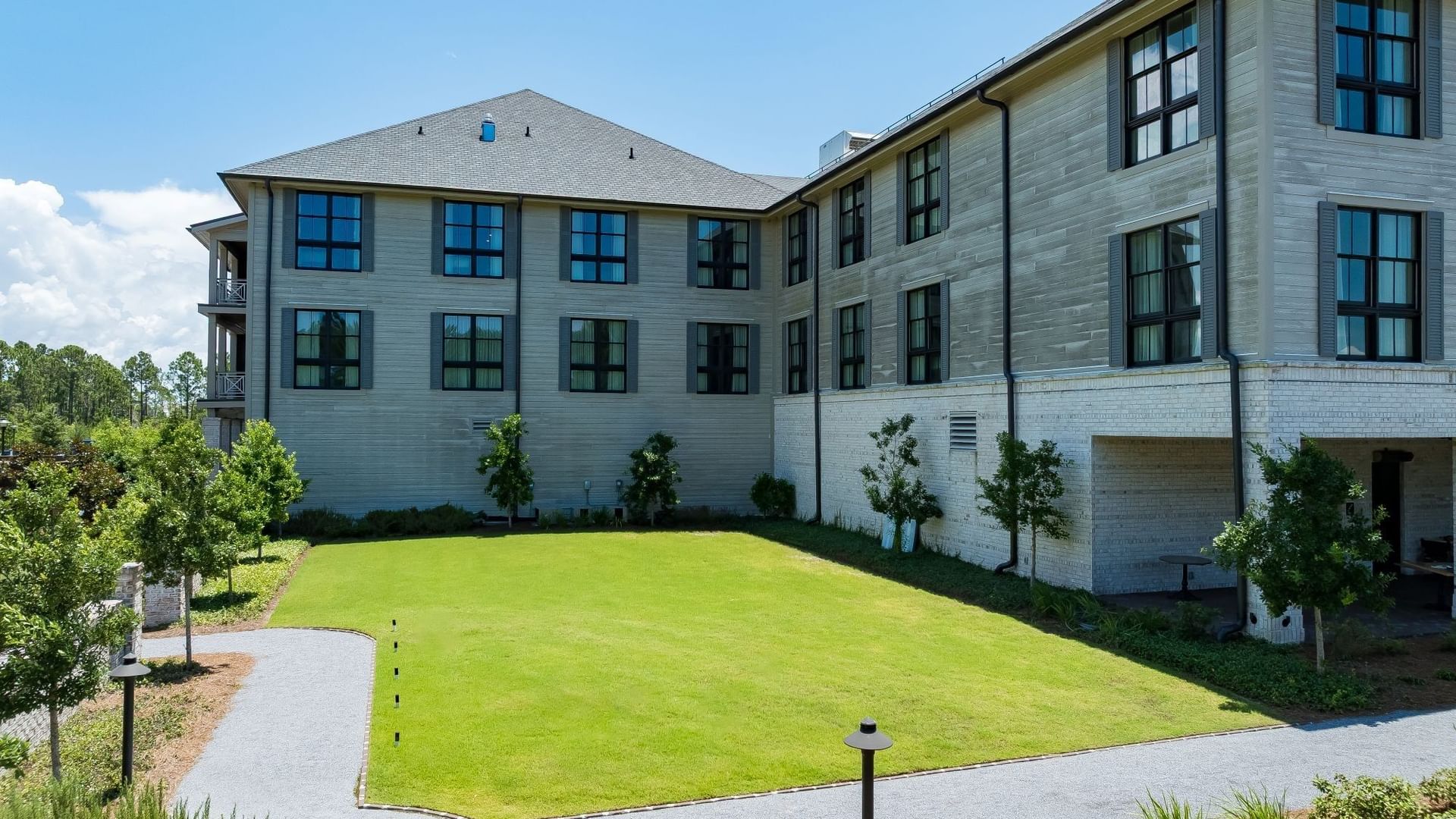 Magnolia Lawn with lush green grass and paved walkways beside a modern building at Camp Creek Inn in Inlet Beach.