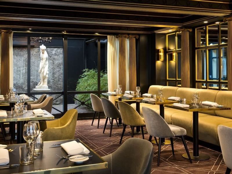 Elegant dining room with velvet seating and courtyard statue view at Hotel Barsey by Warwick