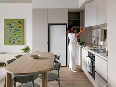 Young woman reaching for item in kitchen with white cabinets and modern decor.