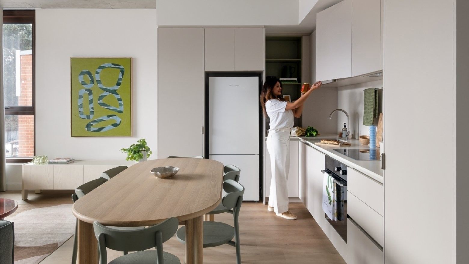 Young woman reaching for item in kitchen with white cabinets and modern decor.