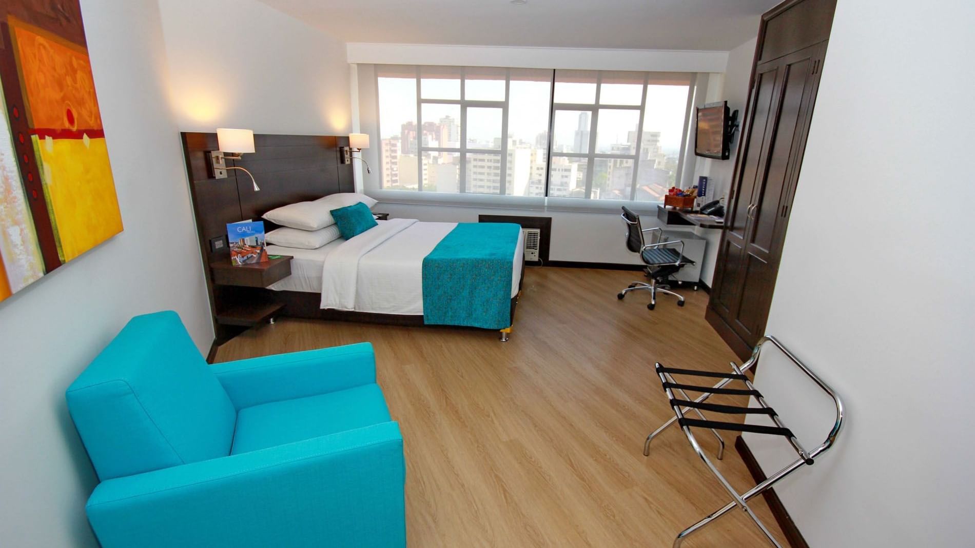 Habitación Dann Cali estándar con cama, almohadas, cuadros en la pared, ventana y decoración en tonos azul y gris en el hotel Dann Carlton Cali: la mejor opción de estadía en Cali.