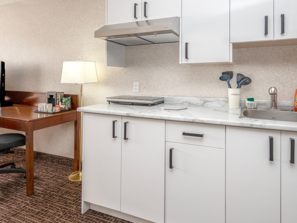 White kitchenette with sink, cabinets, and a desk in a hotel room.