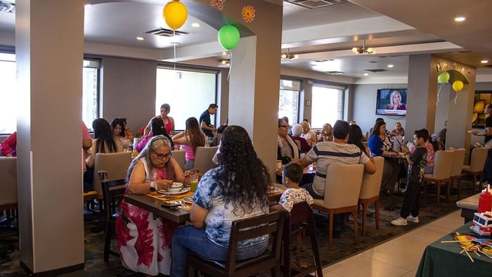 Guests dining at wooden tables in a dining room decorated with balloons in Palmira Cafeteria at Araiza Calafi