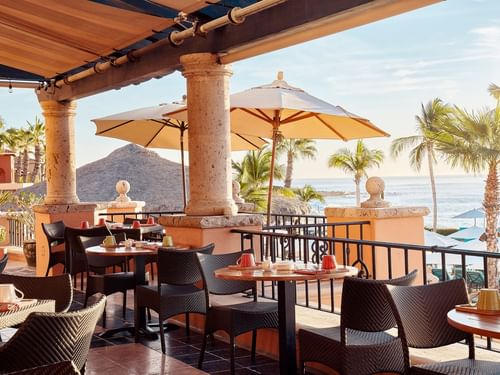 Tomates restaurant dining terrace with tables under umbrellas and sunlit water views at Hacienda del Mar Los Cabos.