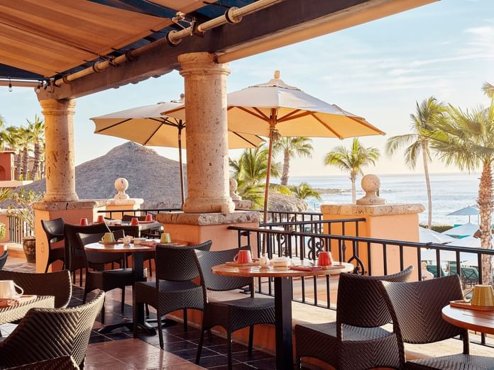 Tomates restaurant dining terrace with tables under umbrellas and sunlit water views at Hacienda del Mar Los Cabos.