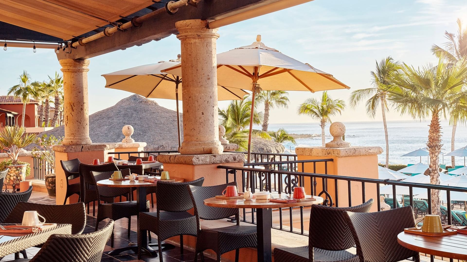 Tomates restaurant dining terrace with tables under umbrellas and sunlit water views at Hacienda del Mar Los Cabos.