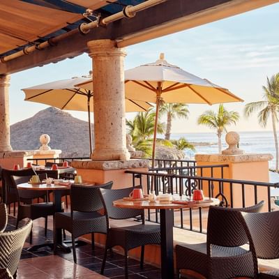 Tomates restaurant dining terrace with tables under umbrellas and sunlit water views at Hacienda del Mar Los Cabos