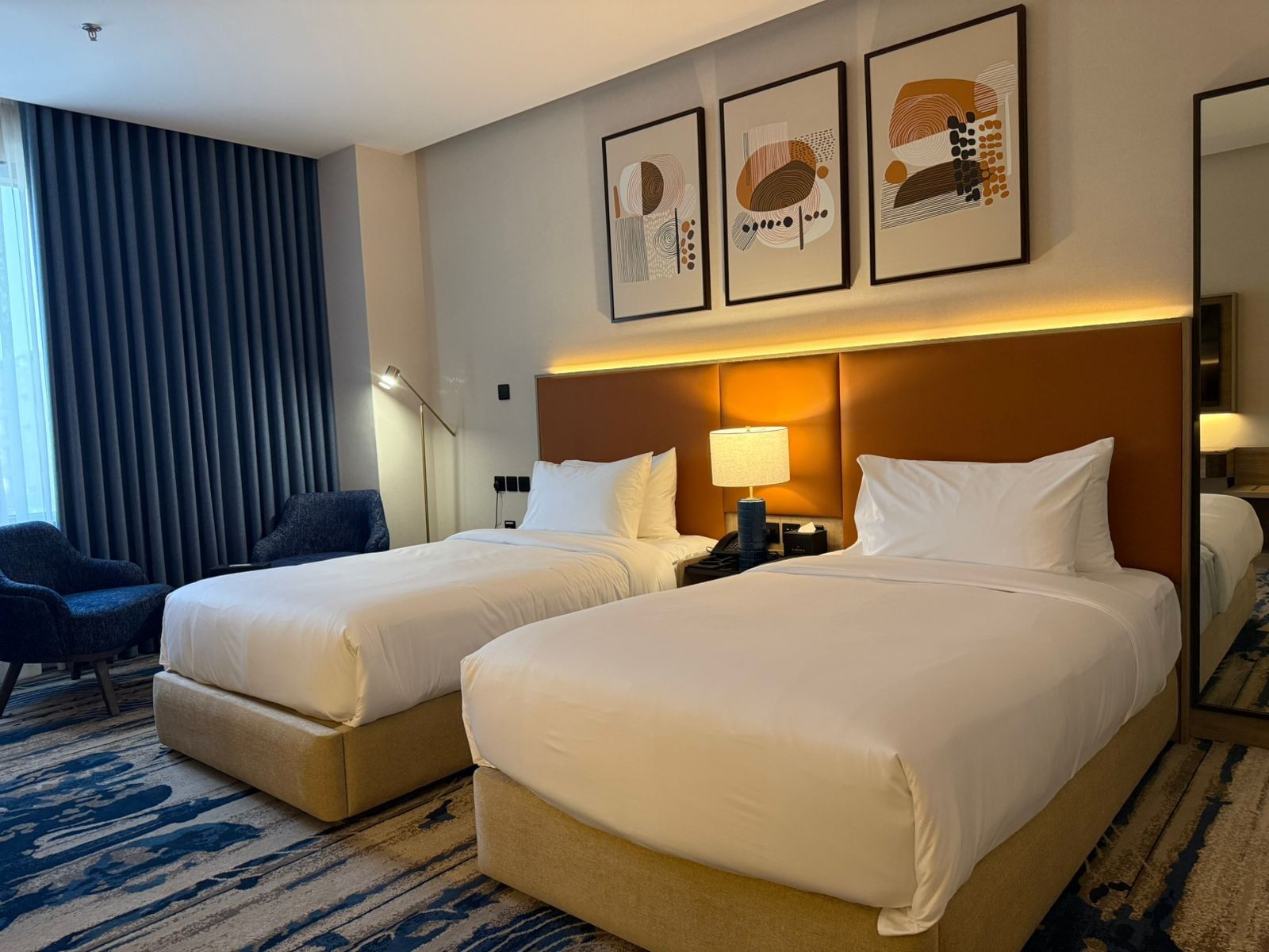 Two beds under wall art and couches near the window in Standard Room at Warwick Jeddah Hotel & Spa