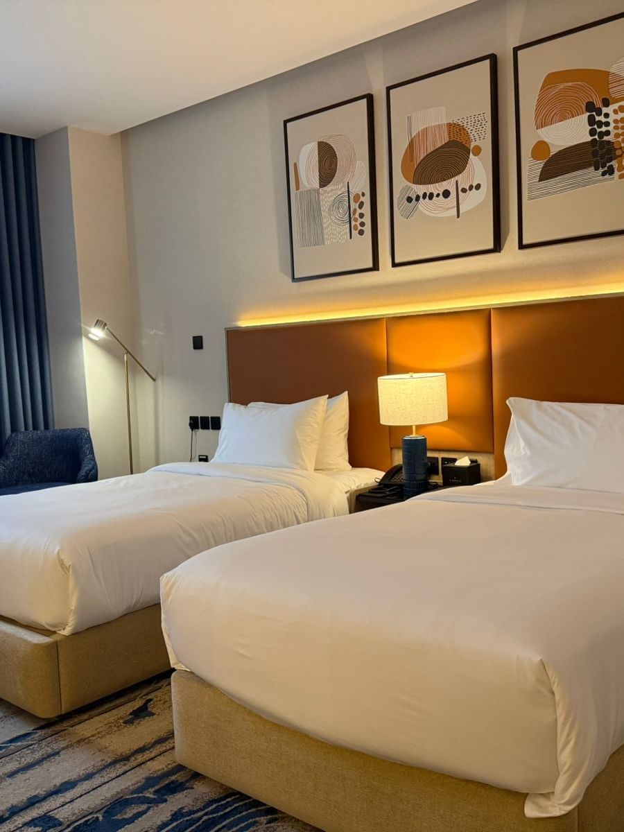 Two beds under wall arts and couches near the window in Deluxe Room at Warwick Jeddah Hotel & Spa