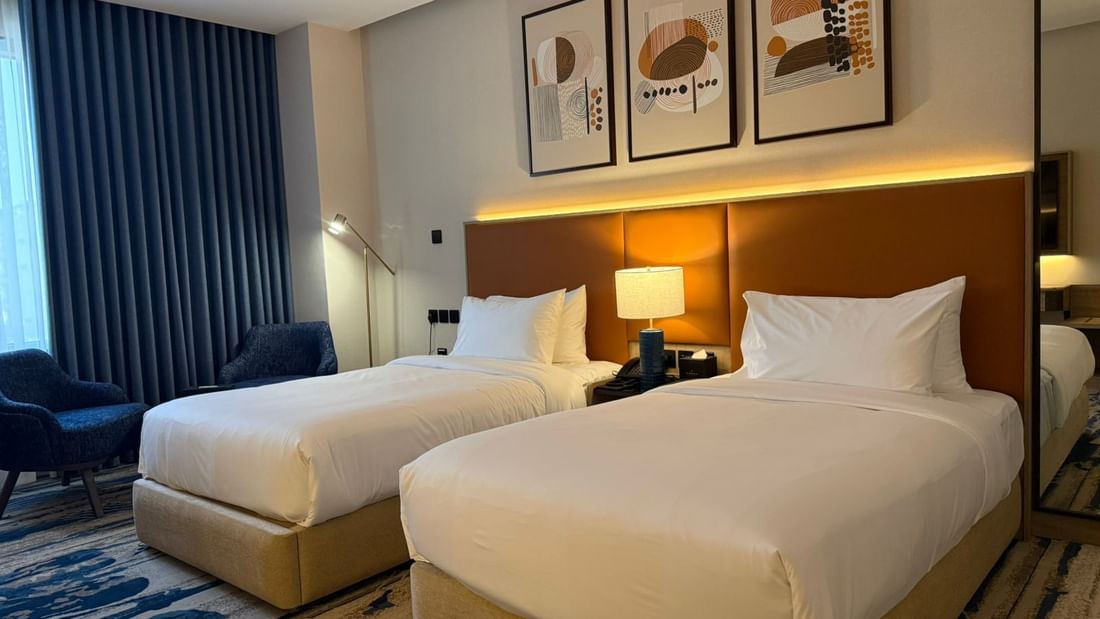 Two beds under wall arts and couches near the window in Deluxe Room at Warwick Jeddah Hotel & Spa