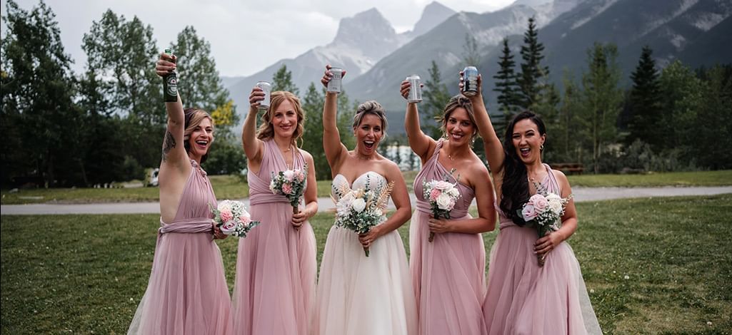A bridal party holds bouquets and beers, toasting the new bride and groom in Canmore.
